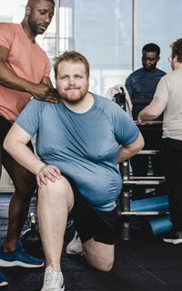 A coach in a gym helps a man position his body correctly while doing a lunge.