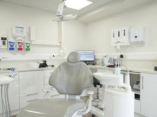 An empty chair in a dental practice, with a sink and dental equipment behind.