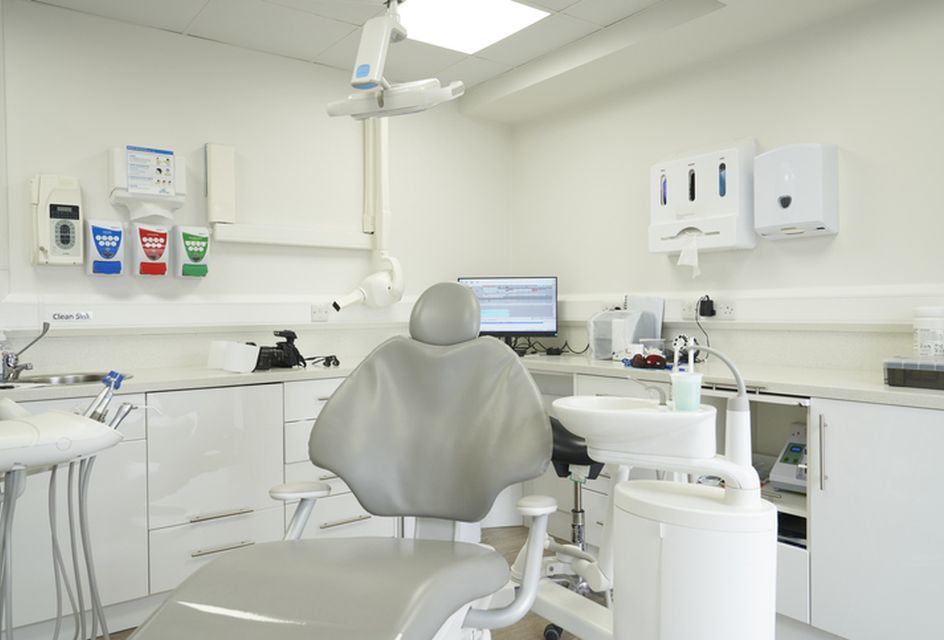 An empty chair in a dental practice, with a sink and dental equipment behind.